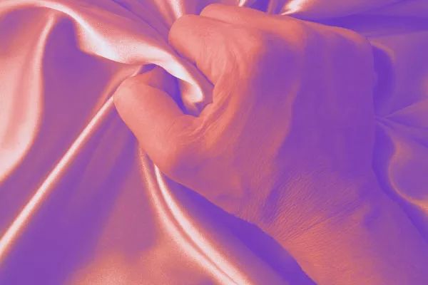 mans hand gripping satin sheets.